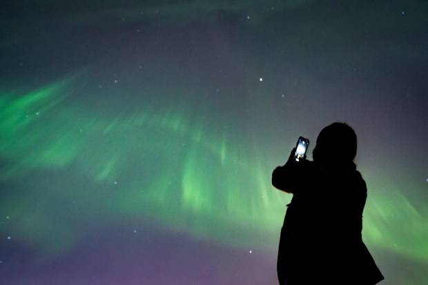 A person takes a photo of Aurora Borealis or the Northern Lights in Vancouver, B.C., Saturday, May. 11, 2024. (Ethan Cairns /The Canadian Press via AP)